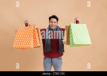 Happy smiling Asian male shopper holding a bunch of shopping bags while looking at camera and happy. Stock Photo
