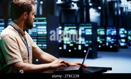 System administrator typing supercomputer hub disaster recovery plan on laptop to provide fast restoration of service, limiting damage and minimizing interruptions to normal operations Stock Photo