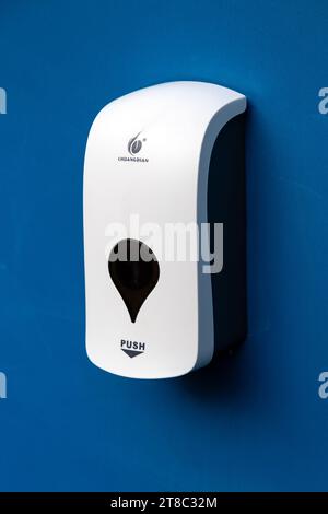 White anti-bacterial hand sanitiser gel dispenser mounted on a blue wall Stock Photo