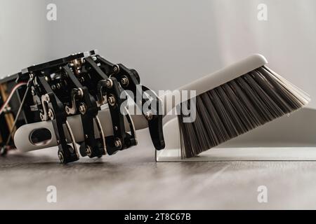 Robotic hand skillfully using a dustpan and brush to sweep the floor Stock Photo