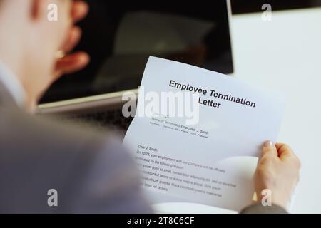 New job. Seen from behind modern 40 years old woman employee in modern green office with laptop and employee termination letter. Stock Photo