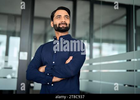 Confident Indian businessman looking away stands in office thinking of success. Stock Photo