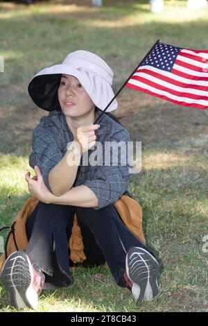 An Asian-American woman sitting on the grass with an American flag at the Long Beach Veterans Day Celebration Stock Photo