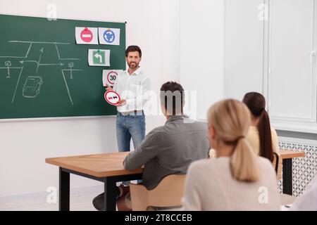 Teacher showing No Overtaking road sign to audience near chalkboard in driving school Stock Photo