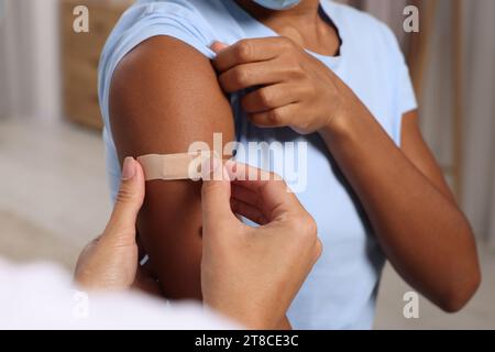 Doctor putting adhesive bandage on young woman's arm after vaccination indoors, closeup Stock Photo