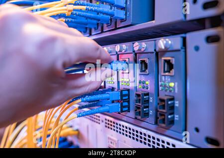man working in network server room with Fiber Optic cables connected to optic ports and UTP Stock Photo