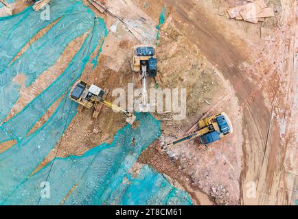 Large tracked excavator with hydraulic hammer breaks asphalt at a construction site Stock Photo