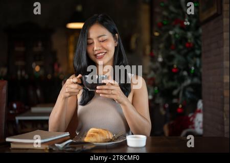 Young rich Asian woman having a hot coffee with breakfast in her elegant home with Christmas decoration. Stock Photo