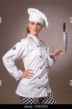 Attractive young female chef balancing a chefs knife on her finger Stock Photo