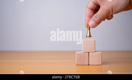 Businessman's hand holding a king placed on the topmost layer of wood. It represents the concept of competition and strategic adjustments for competit Stock Photo