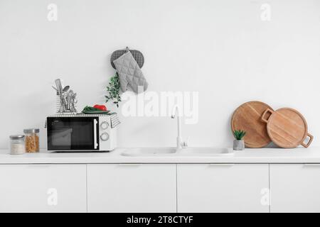 Interior of light kitchen with microwave oven, sink and utensils on white counters Stock Photo