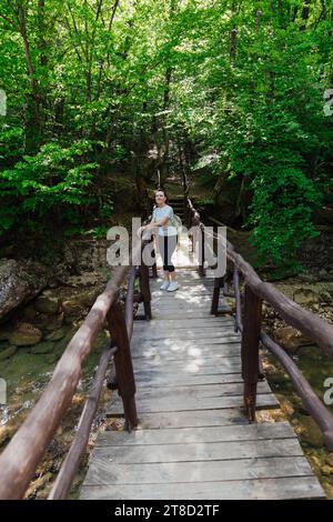 a woman with a backpack stands on a wooden bridge walking in the woods hiking journey Stock Photo