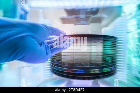 Gloved Hand Holding a Silicon Wafer in plastic holder box used in electronics for the fabrication of integrated circuits Stock Photo