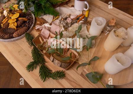 On wooden table are rustic materials for creative decoration of Christmas interior. Fir branches white candles, eucalyptus pine cones dried oranges. W Stock Photo