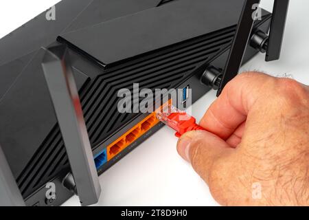 Man's hand plugging internet cable into wifi router Stock Photo