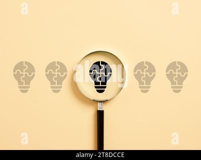 Finding a business idea. Creative idea generation. Analyzing and choosing the best solution. Light bulb symbol with magnifier. Stock Photo