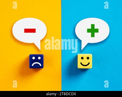 Positive versus negative thinking or mindset. Cubes with happy and unhappy faces with plus and minus symbols in speech bubbles. Stock Photo