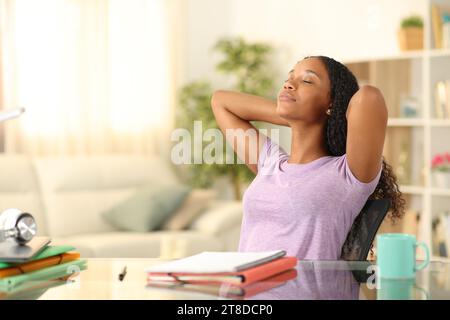 Black student relaxing sitting on a chair with arms on head at home Stock Photo