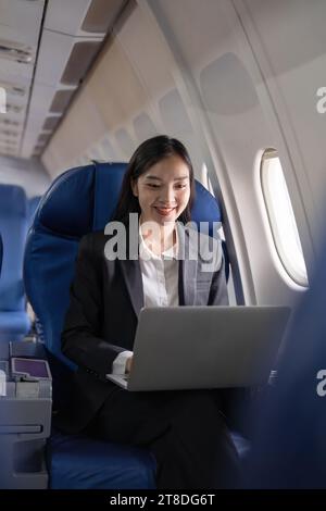 Traveling and technology. Flying at first class. Pretty young Asian business woman using laptop while sitting in airplane Stock Photo