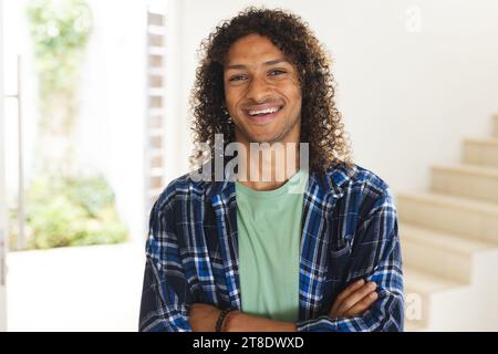 Happy biracial man with long dark curly hair laughing in sunny living room at home Stock Photo
