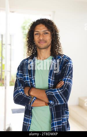 Happy biracial man with long dark curly hair smiling in sunny living room at home Stock Photo