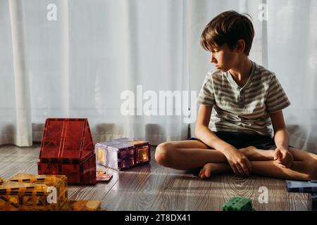 Sad boy sitting on the floor with a designer in the kids room Stock Photo