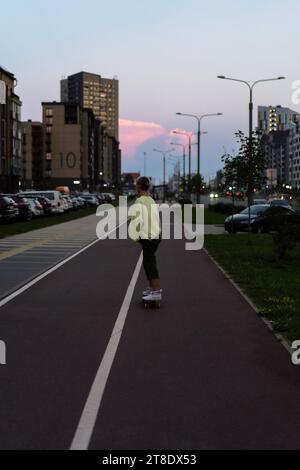 A young woman rides a longboard along the city streets. Stock Photo