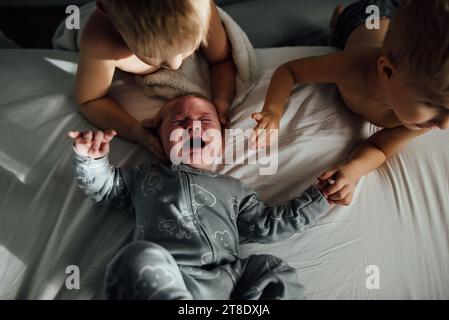 Overhead shot of baby laying on bed while brothers stand over hi Stock Photo