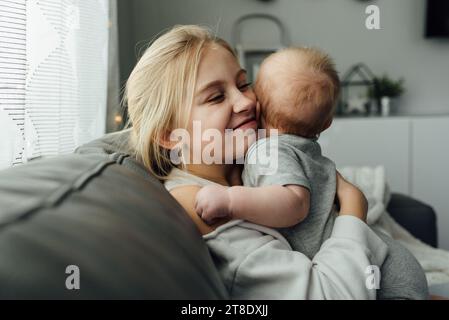 Close up of teen girl sitting on couch smiling and hugging baby Stock Photo
