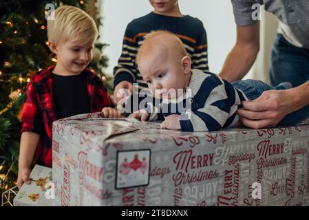 Baby boy lays on top of christmas present while family helps him Stock Photo