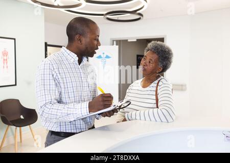 African american male doctor taking notes and talking with senior woman in hospital reception Stock Photo