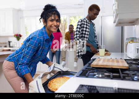 Portrait of happy diverse group of teenage friends cooking and making pizza in kitchen Stock Photo