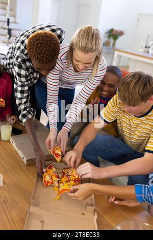 Happy diverse group of teenage friends sitting on couch and sharing pizza Stock Photo