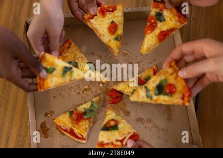 Diverse group of teenage friends sharing pizza on table at home Stock Photo