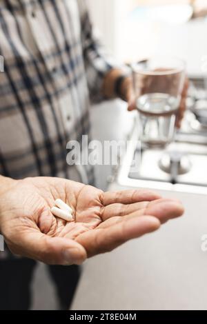 Senior biracial man holding glass of water and taking pills at home Stock Photo