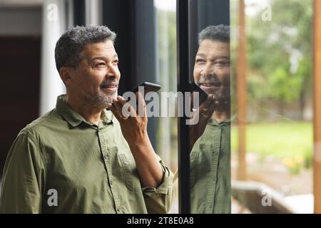 Happy senior biracial man talking on smartphone at window at home Stock Photo