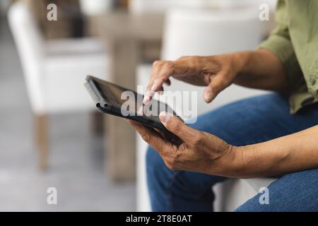 Senior biracial man sitting on table and using tablet at home Stock Photo