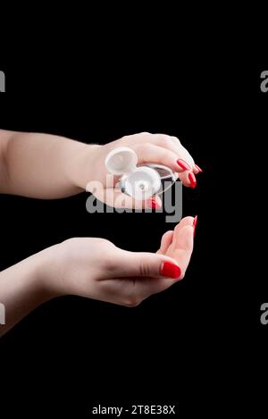 A young woman pours hand sanitizer gel into her palm. Manicure, black background, health, copy space. Stock Photo