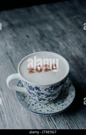 closeup of cappuccino with the number 2024, as the new year, on its milk foam, served on a white ceramic cup, with a blue floral pattern, placed on a Stock Photo