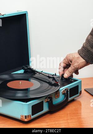 Close up vertical photo, hand of senior adult male, Caucasian, preparing vinyl, in the record player in the form of blue suitcase. Concept hobbies. Stock Photo