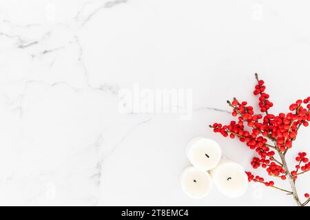 Minimal Christmas decorations candles and branch with red berries on white marble table background. Christmas, New Year, winter concept. Flat lay, top Stock Photo