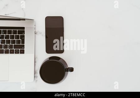 Minimal white office desk table with laptop computer, smartphone with black screen and cup of coffee. Top view. Copy space, flat lay. Stock Photo