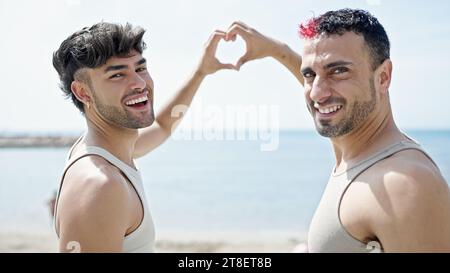 Two men couple hugging each other doing heart gesture at seaside Stock Photo