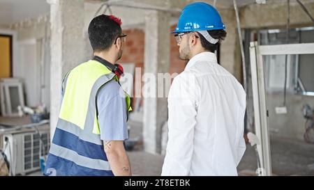 Two men builder and architect standing together backwards at construction site Stock Photo