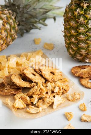 Yellow organic dried sweet pineapple slices and circles on baking paper on light table with raw pineapples. Stock Photo