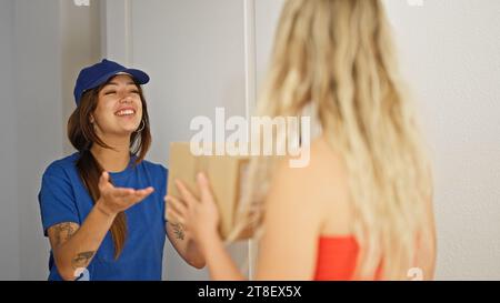 Young beautiful hispanic woman delivery woman giving package to client at home Stock Photo