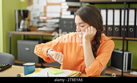 Young beautiful hispanic woman business worker looking clock with serious face at office Stock Photo