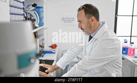 Concentrated middle-aged man with grey hair, immersed in groundbreaking science, harnesses computer power in the buzzing lab environment Stock Photo