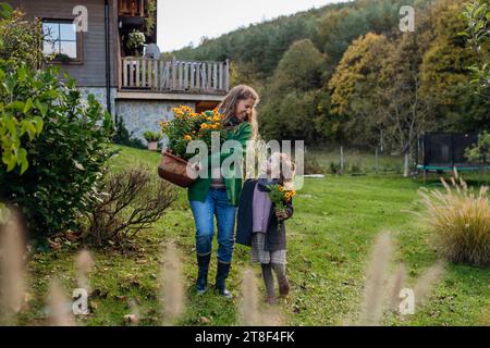 Mother and daughter taking care of home garden, replanting flowers. Pregnant mother spending time outdoors during cold autumn day. Stock Photo
