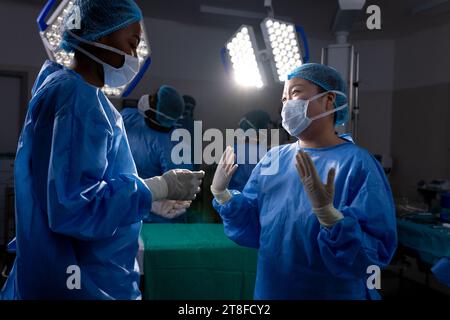 Diverse female doctors with face masks talking in hospital operating room Stock Photo
